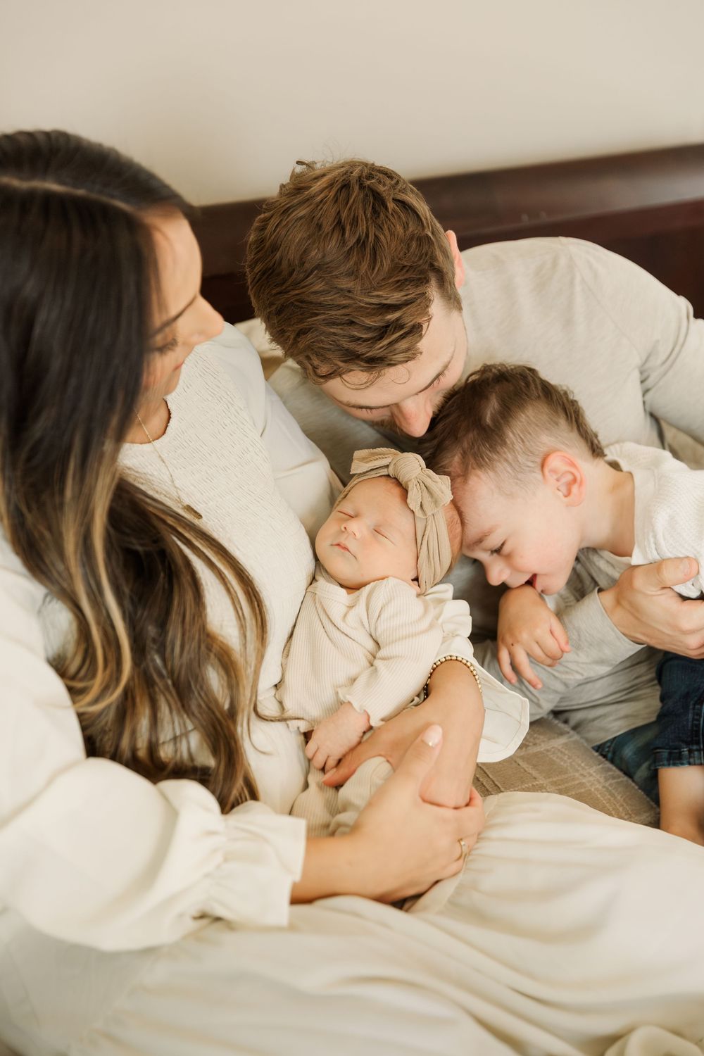 A tender family moment captured in bed as parents snuggle with their sleeping newborn baby under white bedding.