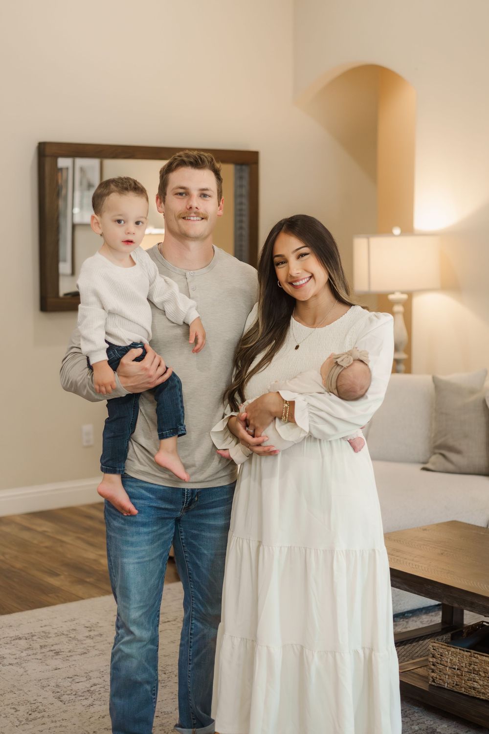 A family in jeans and white outfits shares tender moments together in a bright living room with hardwood floors.