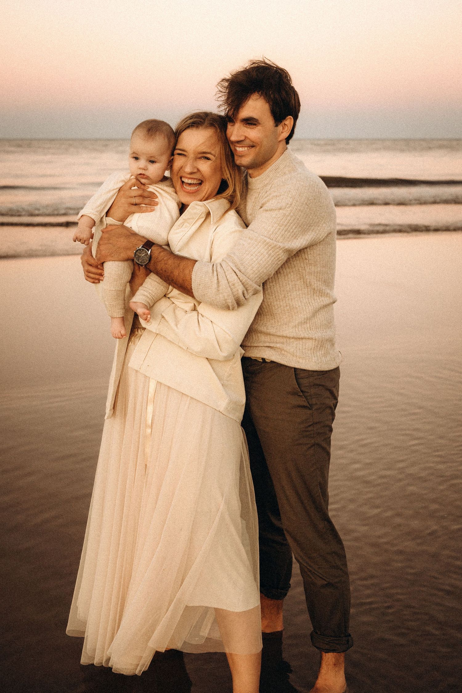 A family shares joyful moments together during sunset at the beach in matching cream-colored outfits. Javea photographer