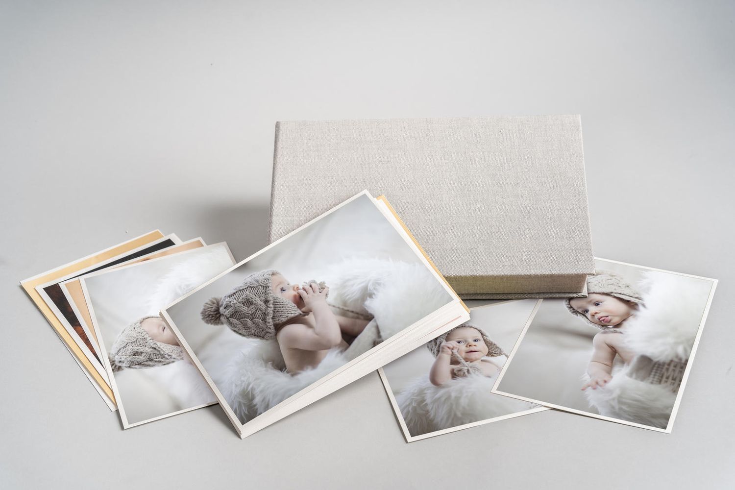 Professional photo prints and albums displayed on a light gray surface with soft neutral tones and delicate styling.