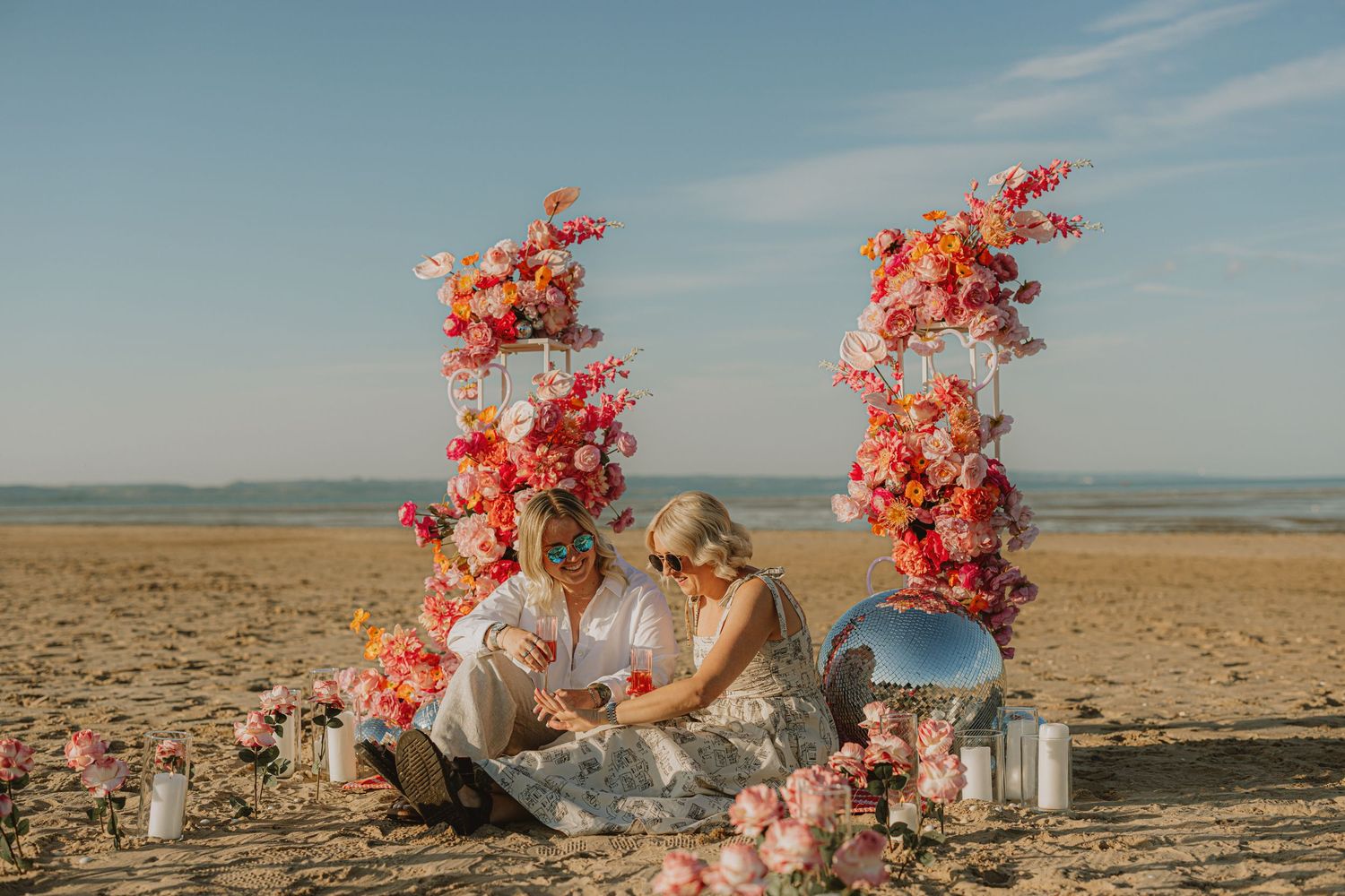 Beach ceremony setup with vibrant coral flower arrangements and decorative elements at golden hour.