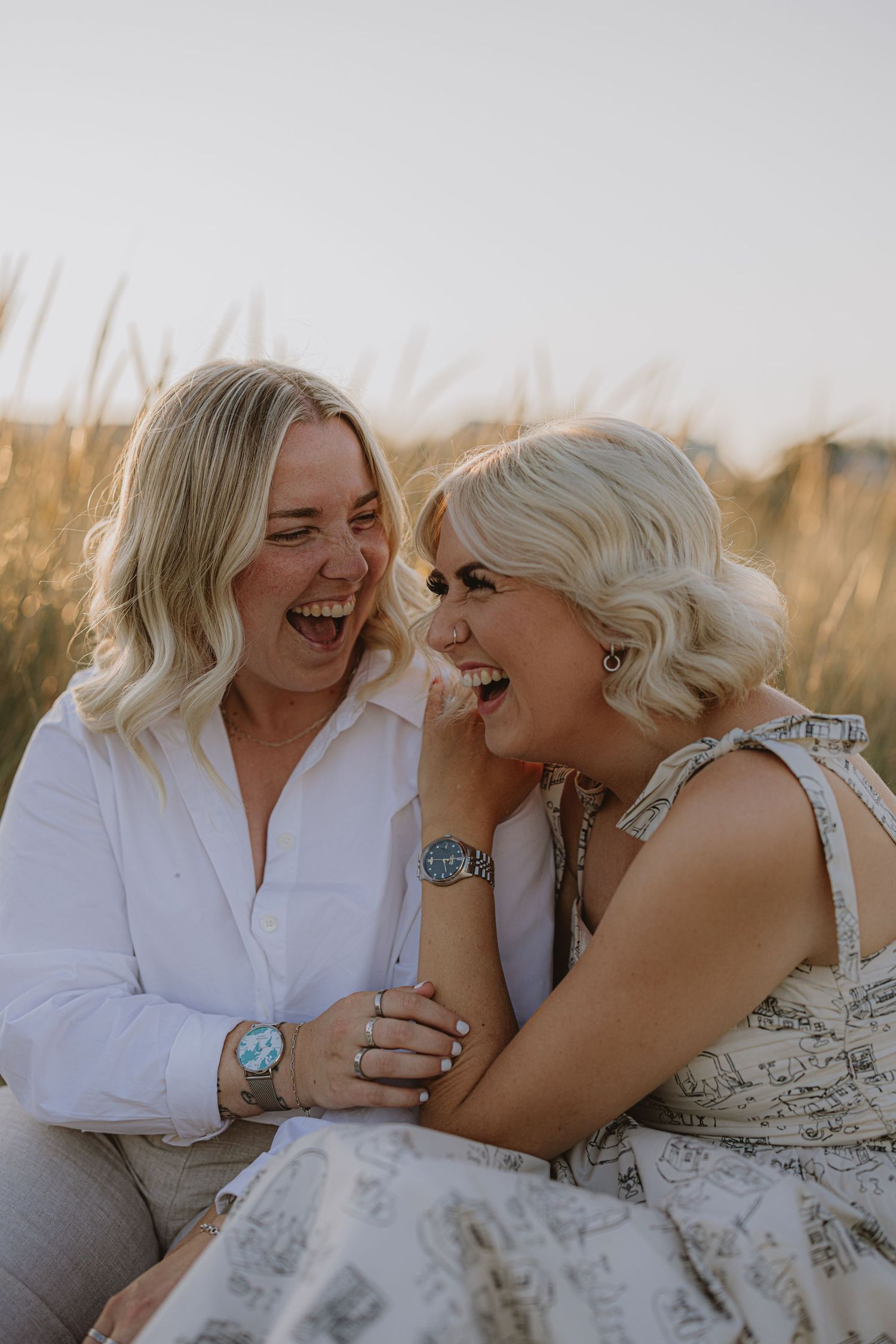 Two people sharing joyful laughter while lying on sand during a beach photoshoot.