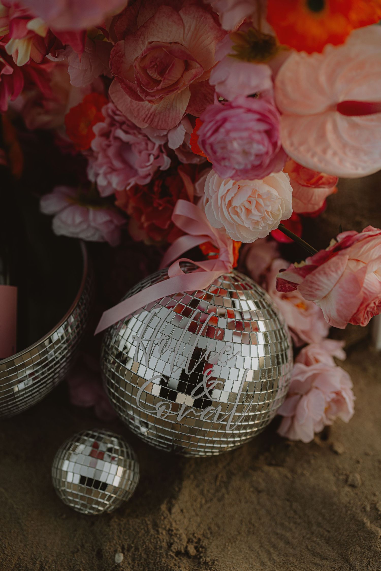 Disco balls and pink flowers create a glamorous beach party decoration setup.