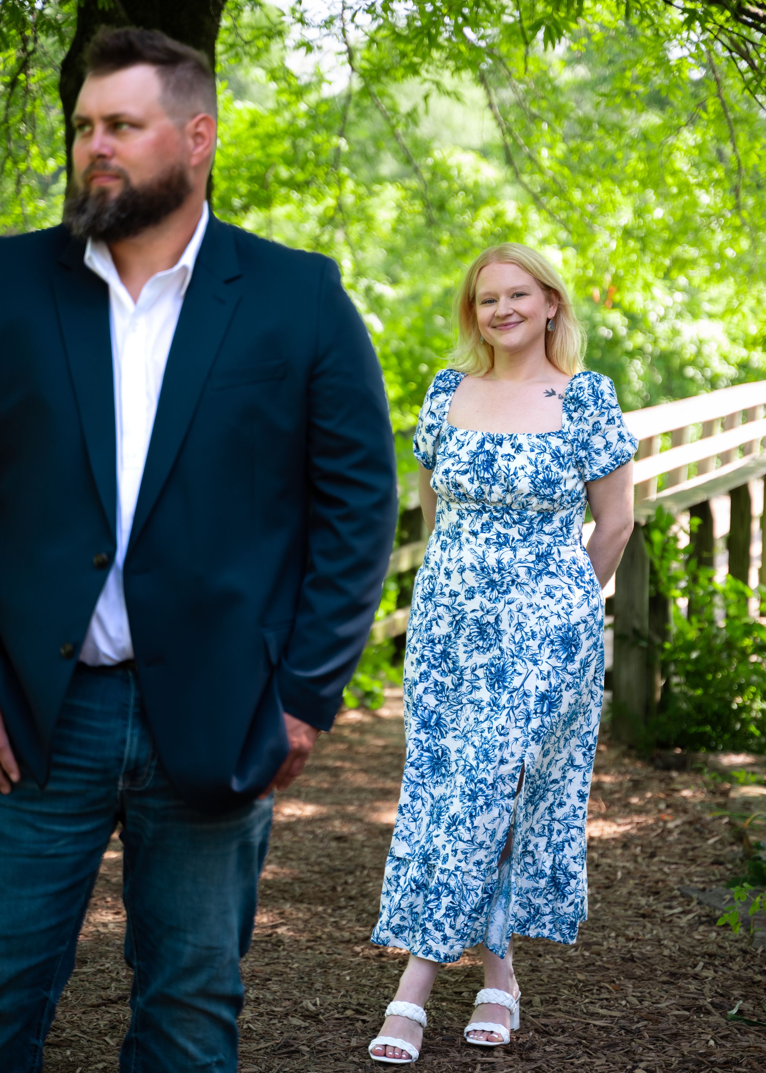 A couple in formal attire poses together on a wooded path during a photo shoot.