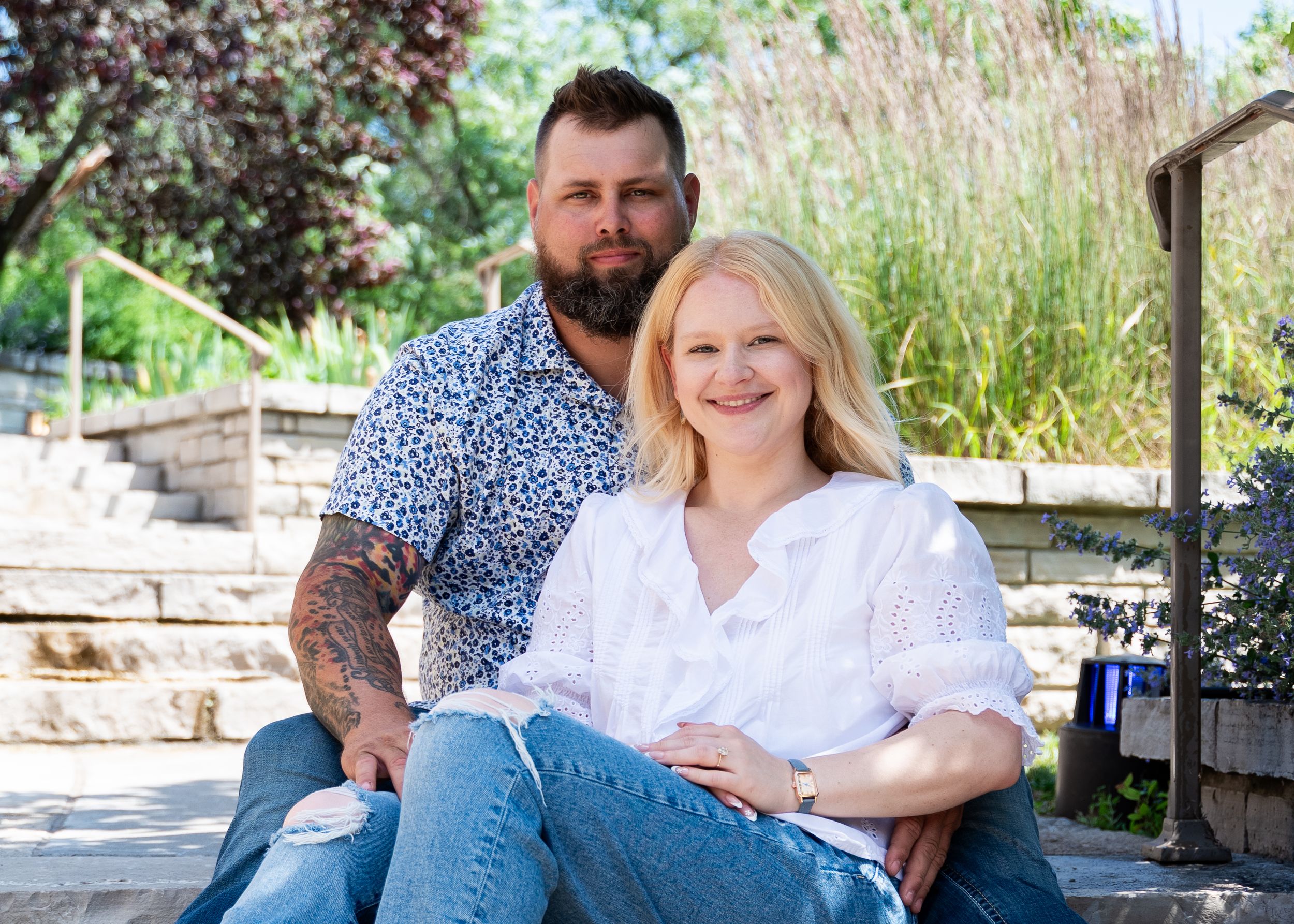 Casual outdoor portrait of couple sitting on wooden bench in garden setting.