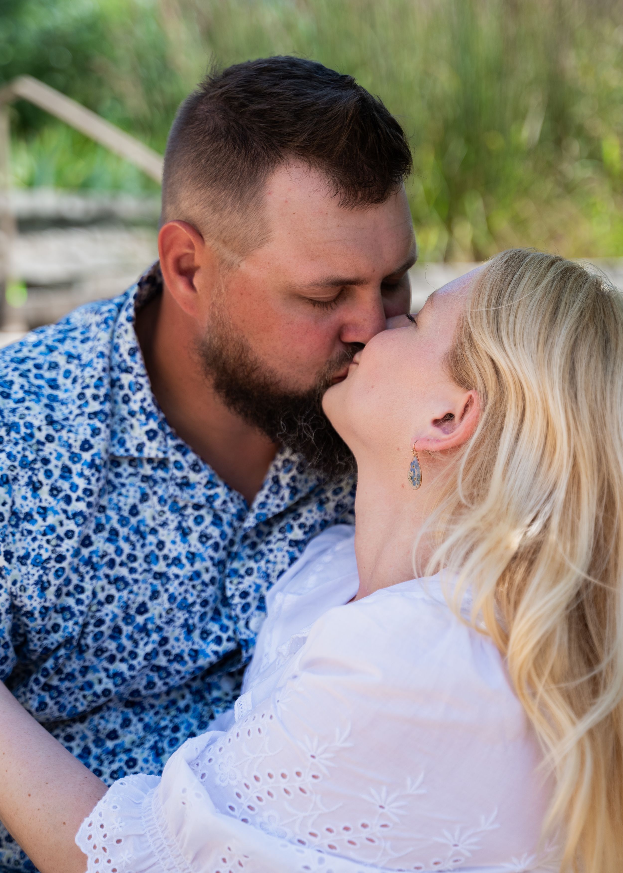 Intimate moment captured between couple in white and blue floral clothing outdoors.