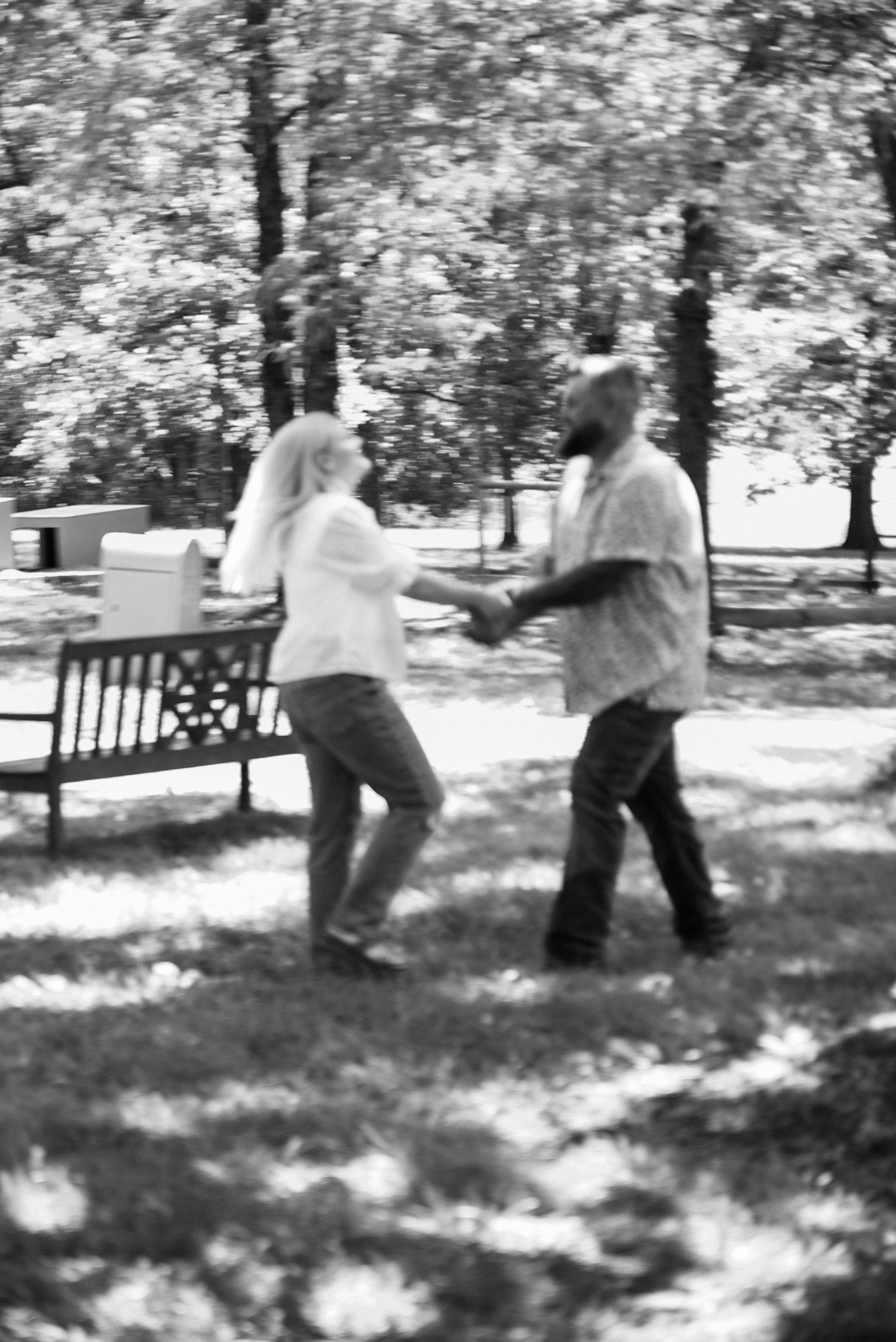 Black and white photo of two people dancing playfully in a park setting.