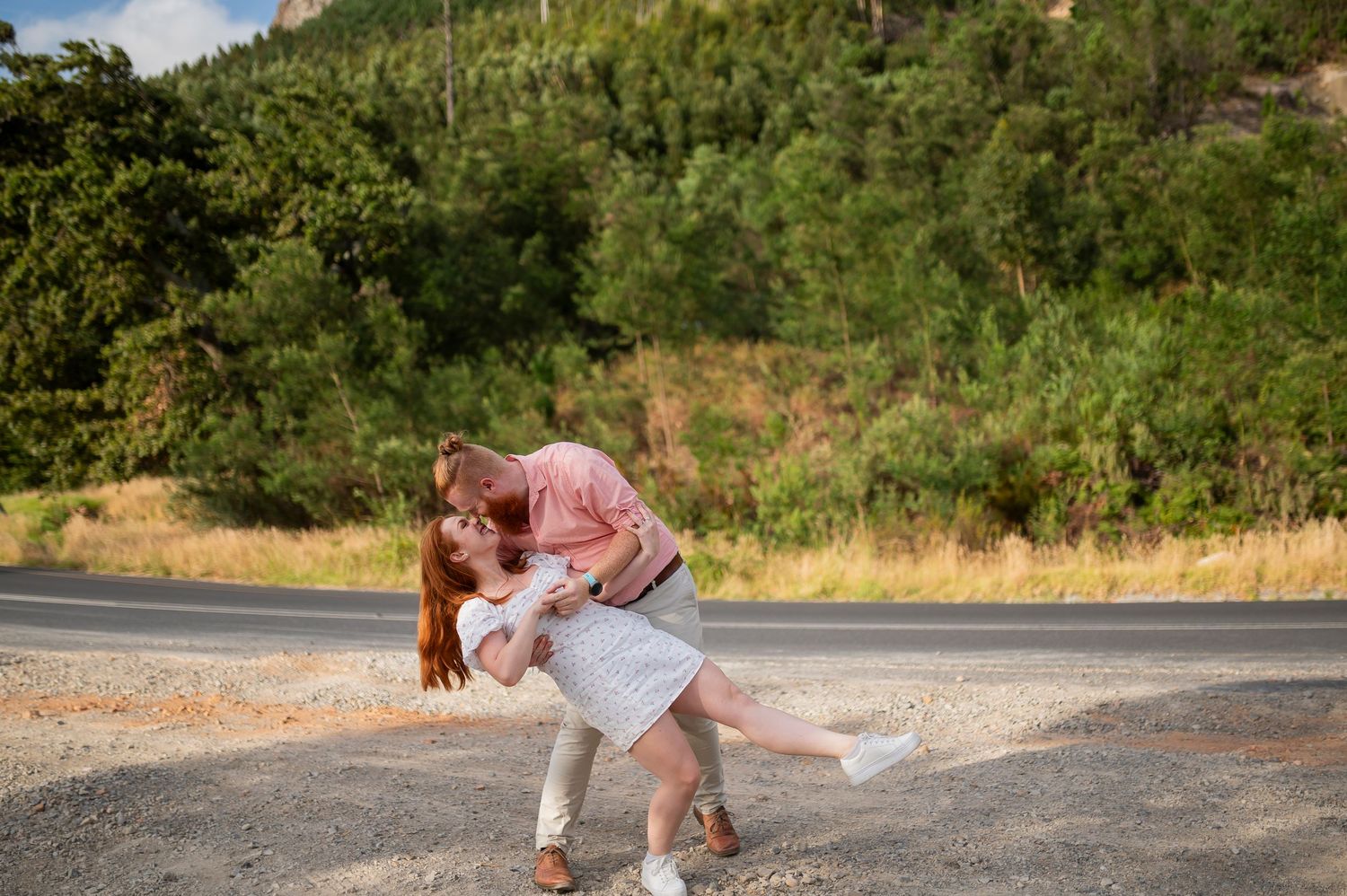 A couple and their dog share a playful moment on a rural road during a warm sunny day.