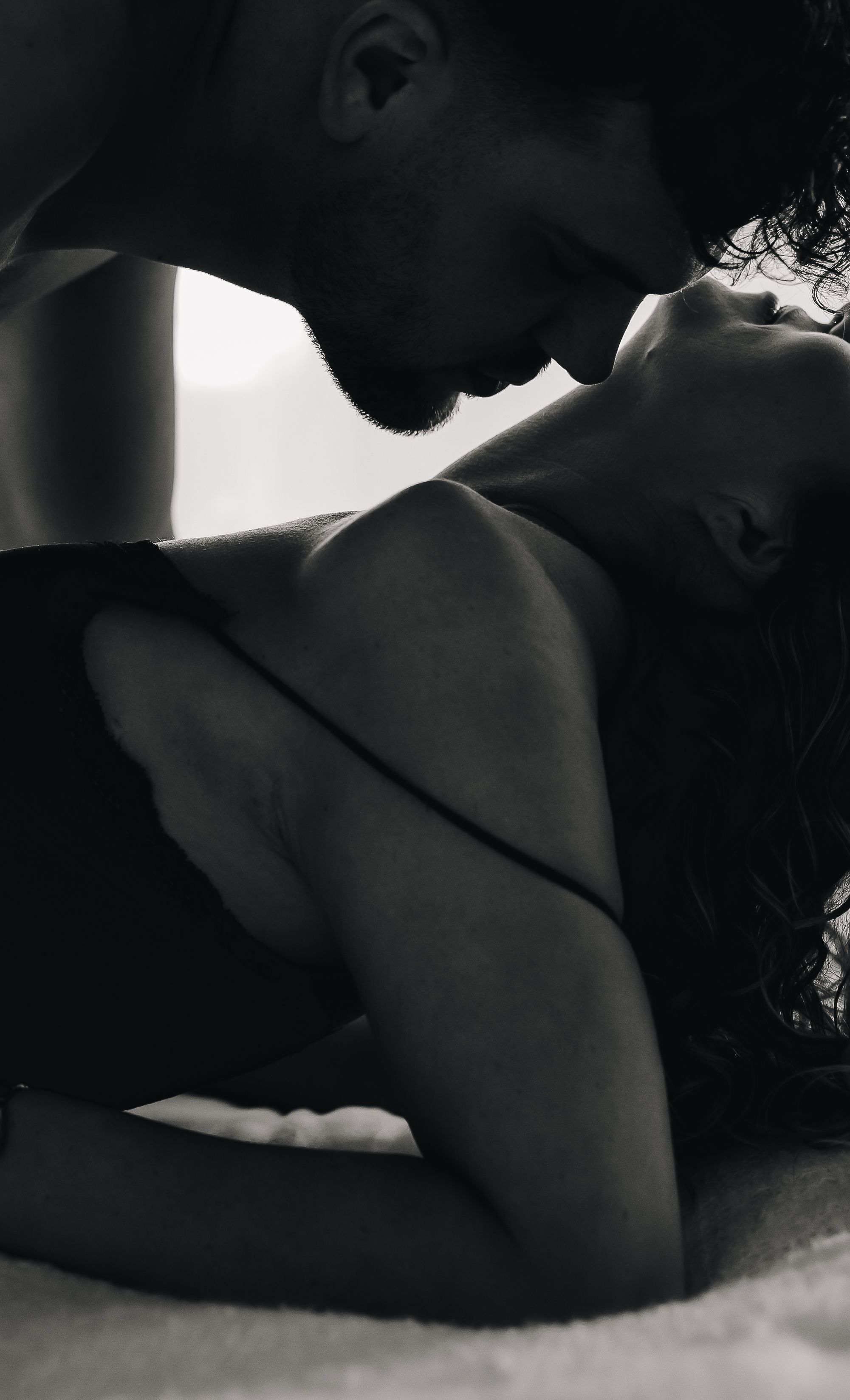 Intimate monochrome photograph showing tender romantic moment between a couple in soft lighting.