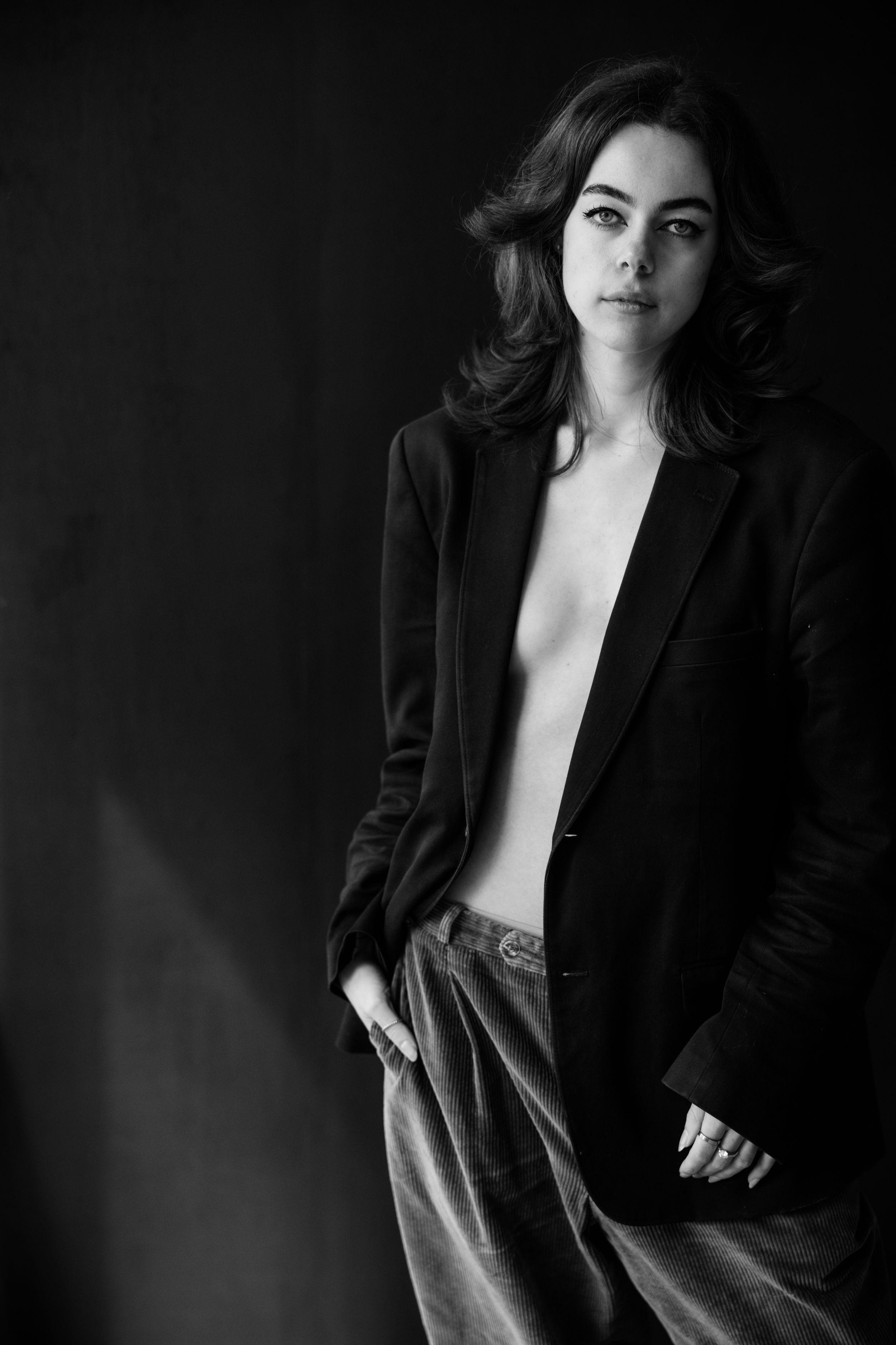 Dramatic black and white portrait photoshoot featuring elegant black blazer styling against dark background.