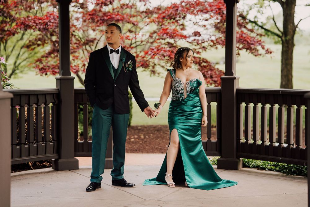 A couple in formal attire poses under a gazebo with blooming red maple trees in the background at Hershey, PA.