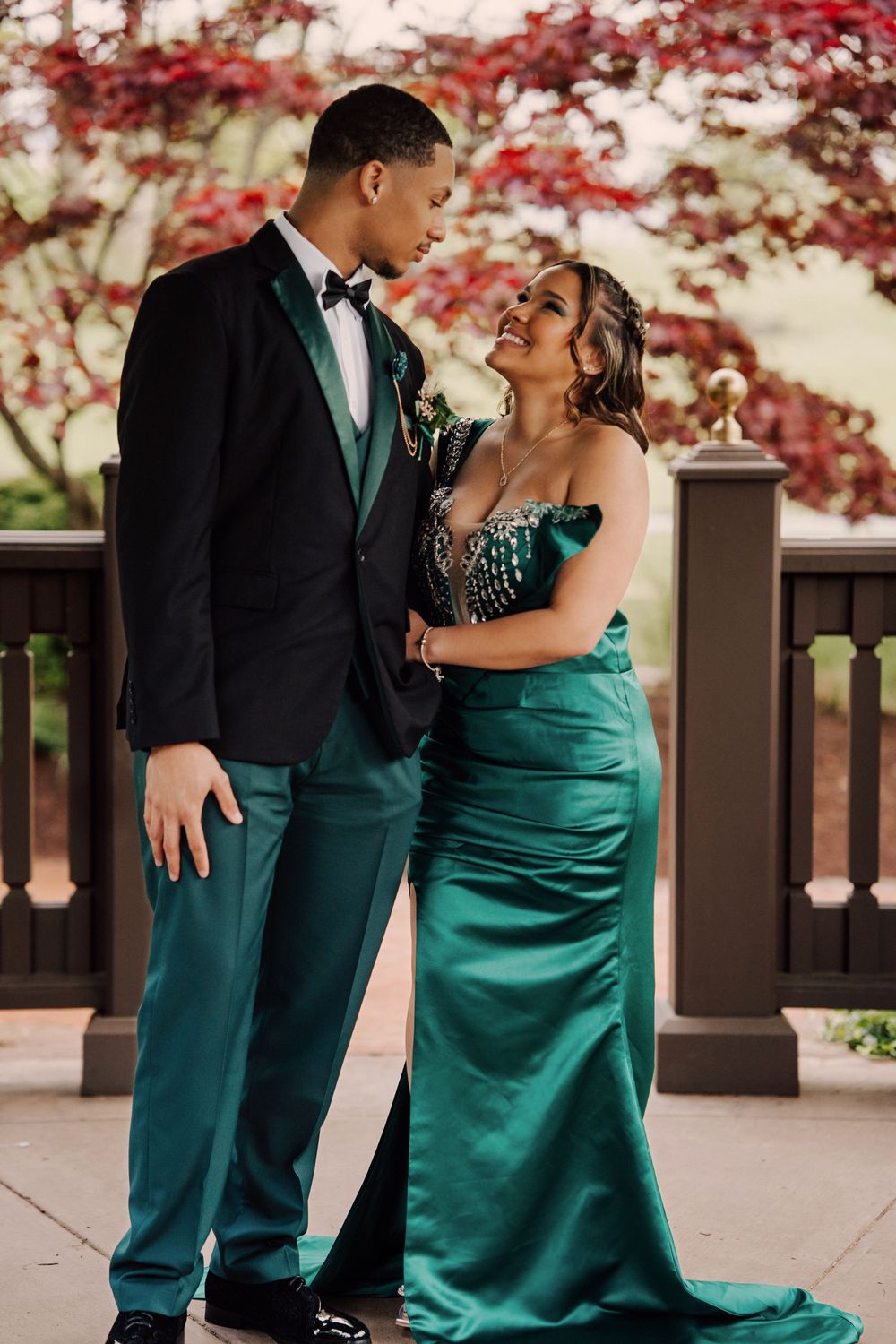 Couple in emerald green and black formal attire sharing romantic moments on an outdoor deck in Hershey, PA.