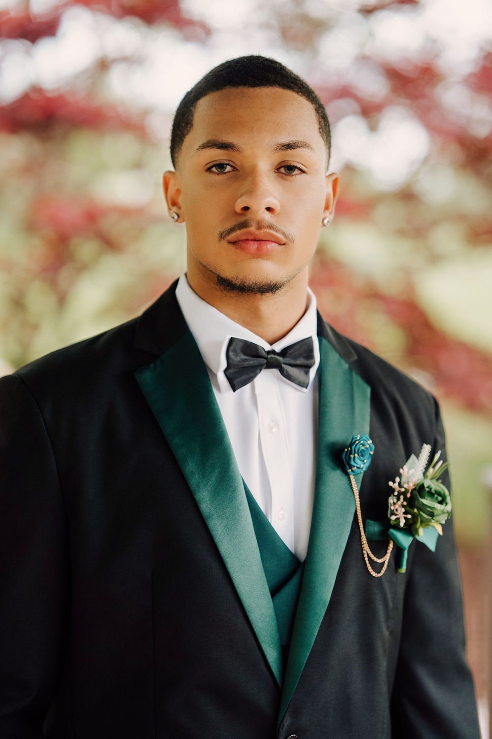 Prom attire of classic black tuxedo with dark green lapels and white bowtie posing for prom photoshoot.