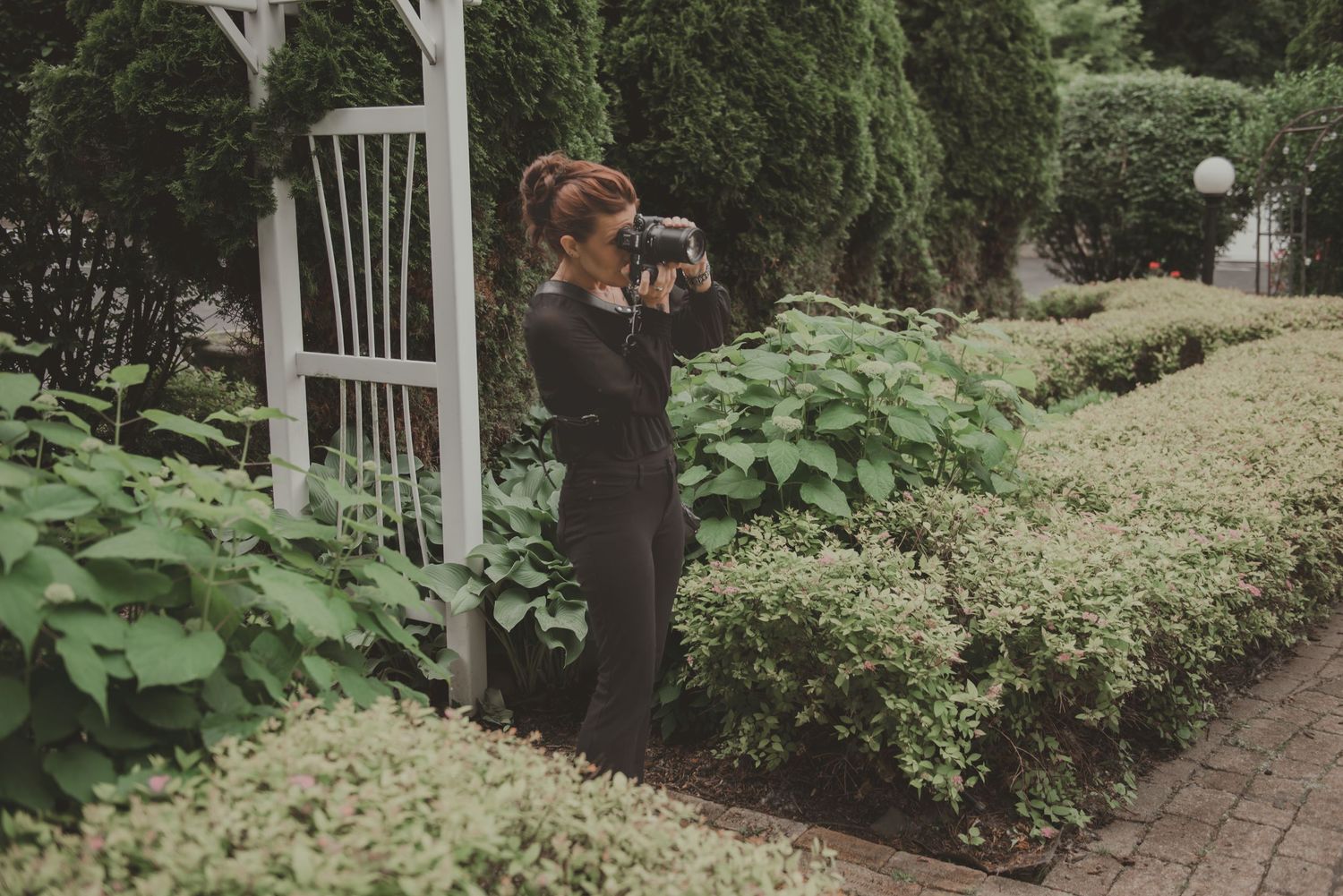 Professional photographer holding camera while leaning against pillar at dusk with cityscape in background.