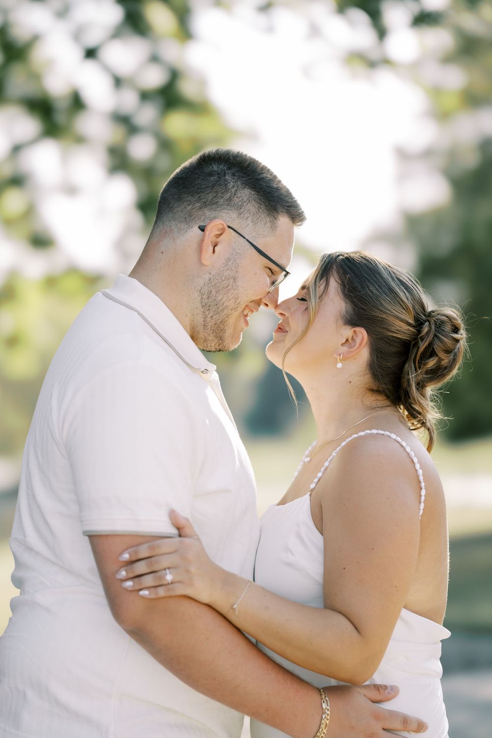 A romantic couple in white outfits embrace tenderly during a wedding photo session outdoors.