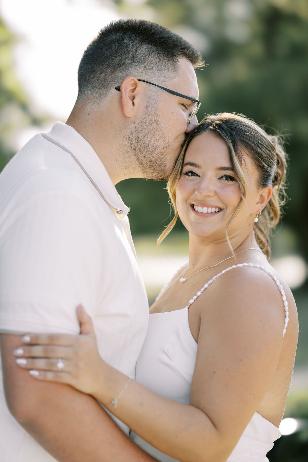 A romantic wedding couple embraces in soft natural lighting while wearing white and cream colored attire.