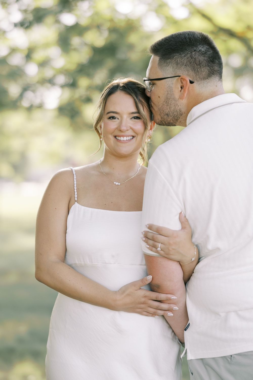 A romantic couple embraces while sharing an intimate moment together in a sun-dappled outdoor setting.