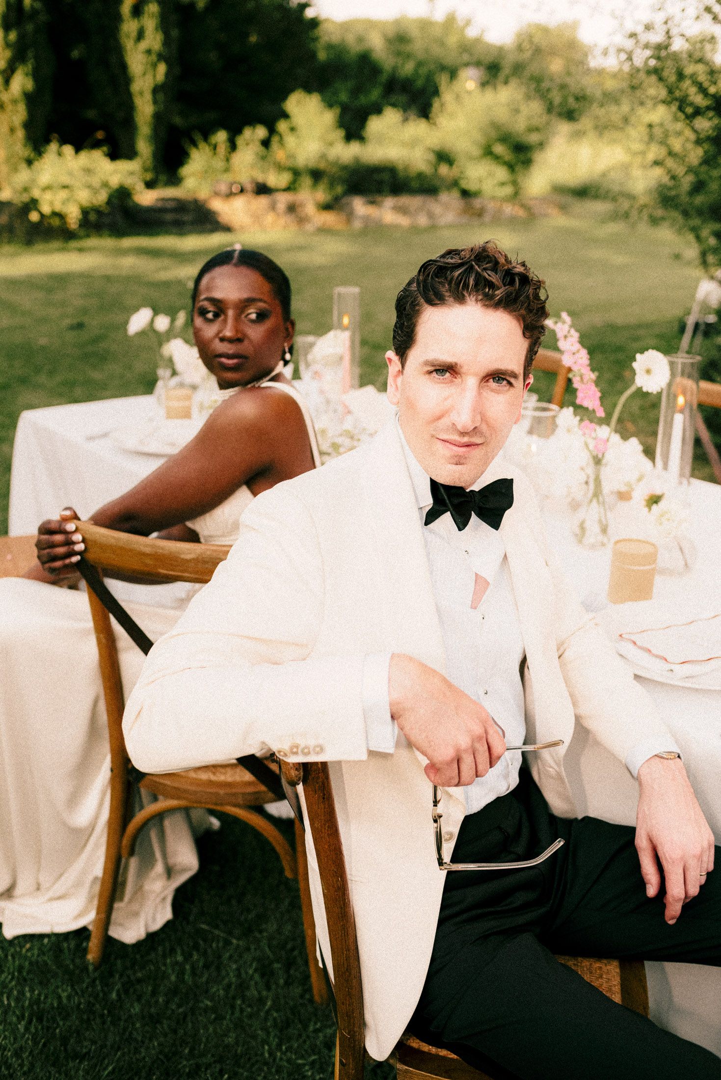 Elegant wedding party members in black and white formal attire seated at outdoor dining tables during sunset.