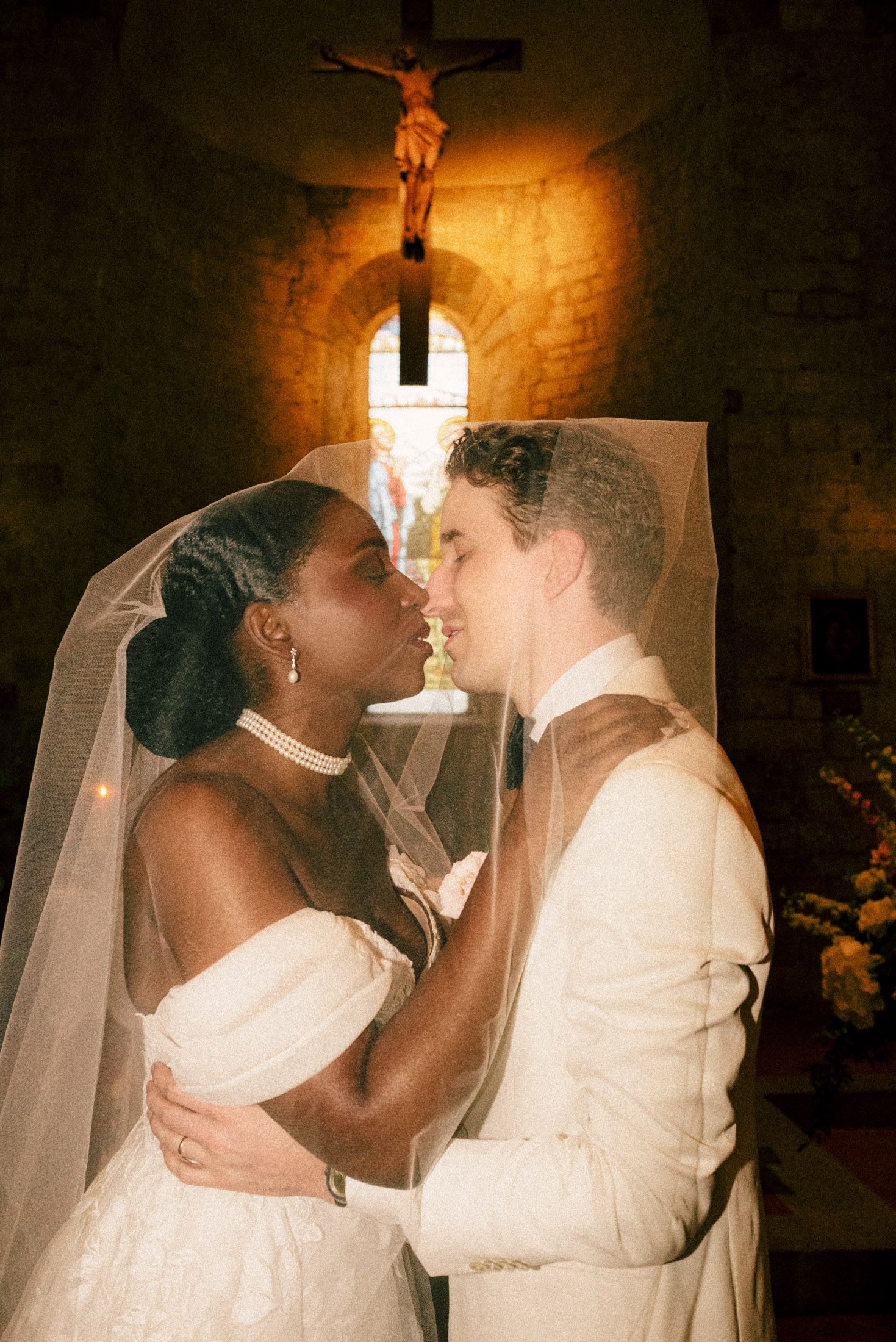 Romantic couple in wedding attire share intimate moments during their church ceremony, lit by warm candlelight.