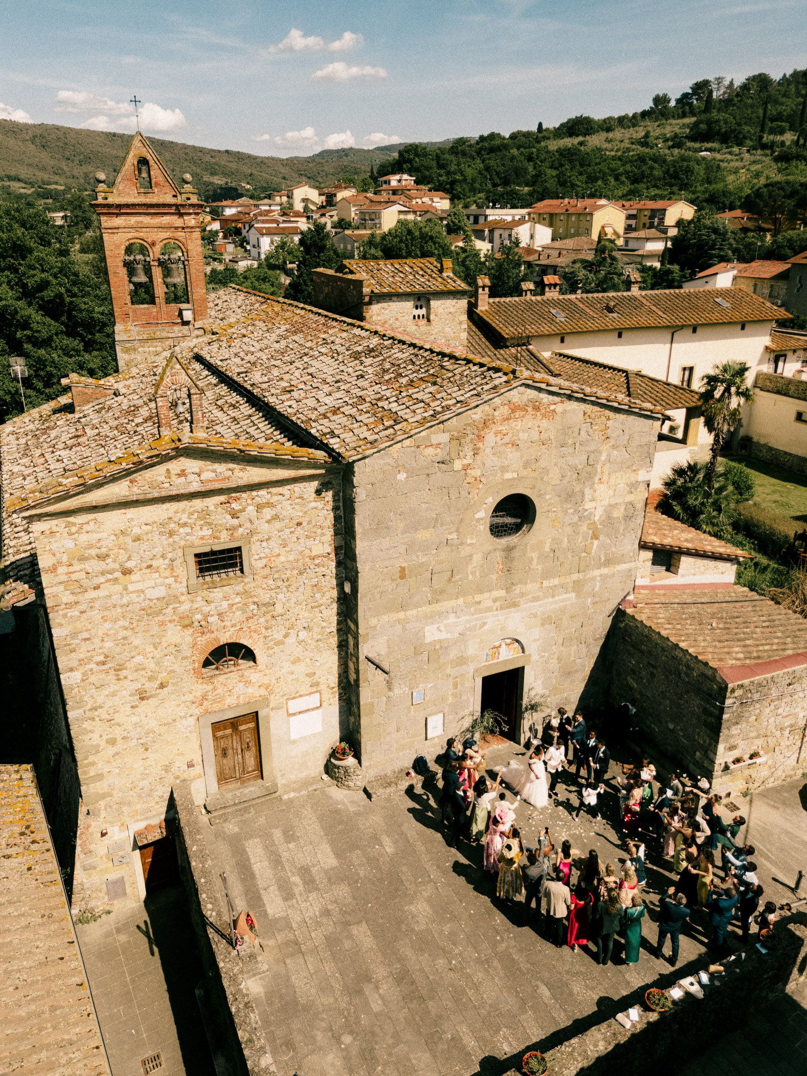 Aerial view of a stone church and historic buildings in an Italian hilltop village on a sunny summer day.