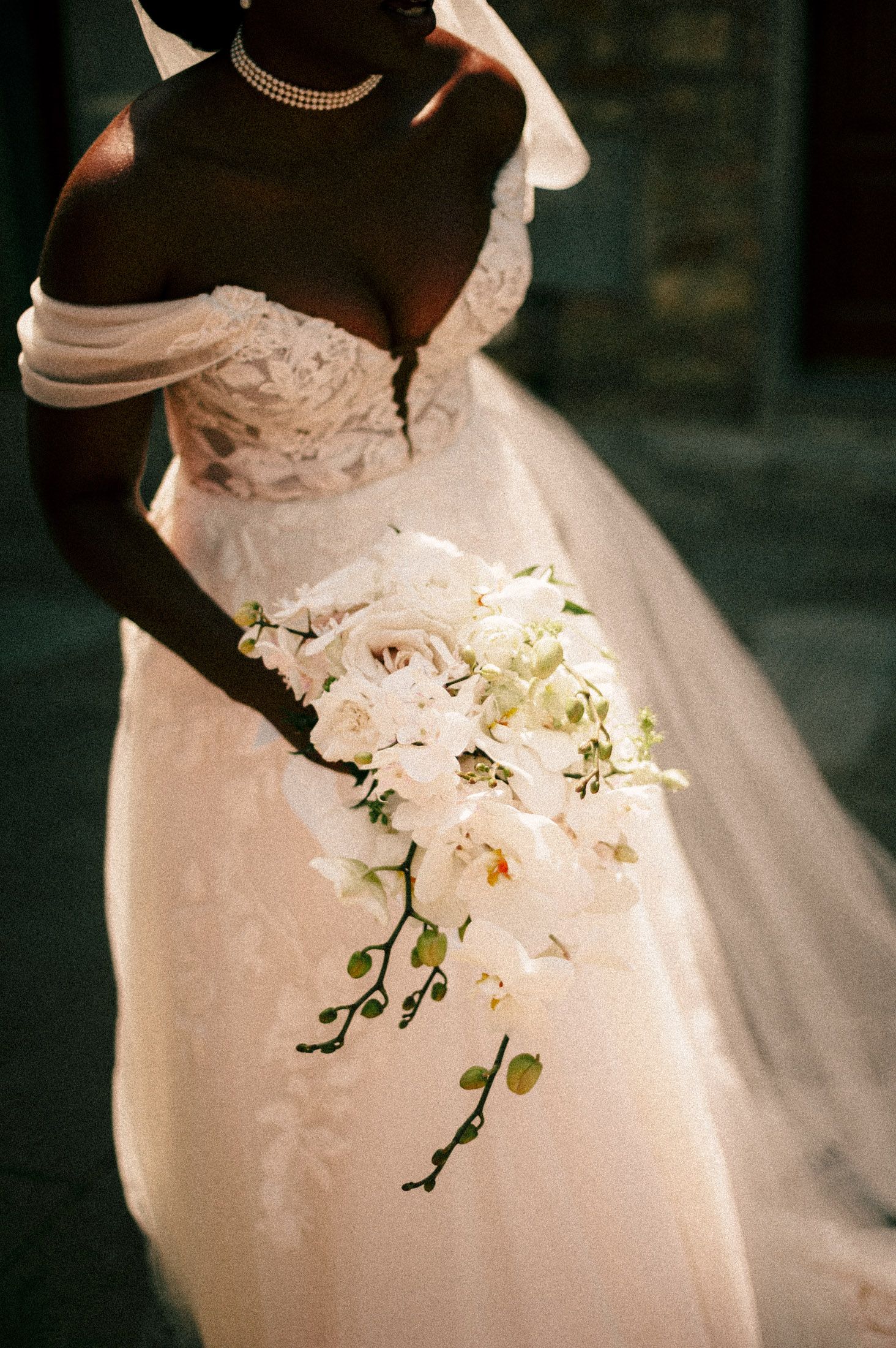 A cascading white orchid wedding bouquet shown in a series of detail shots against a formal white wedding gown.