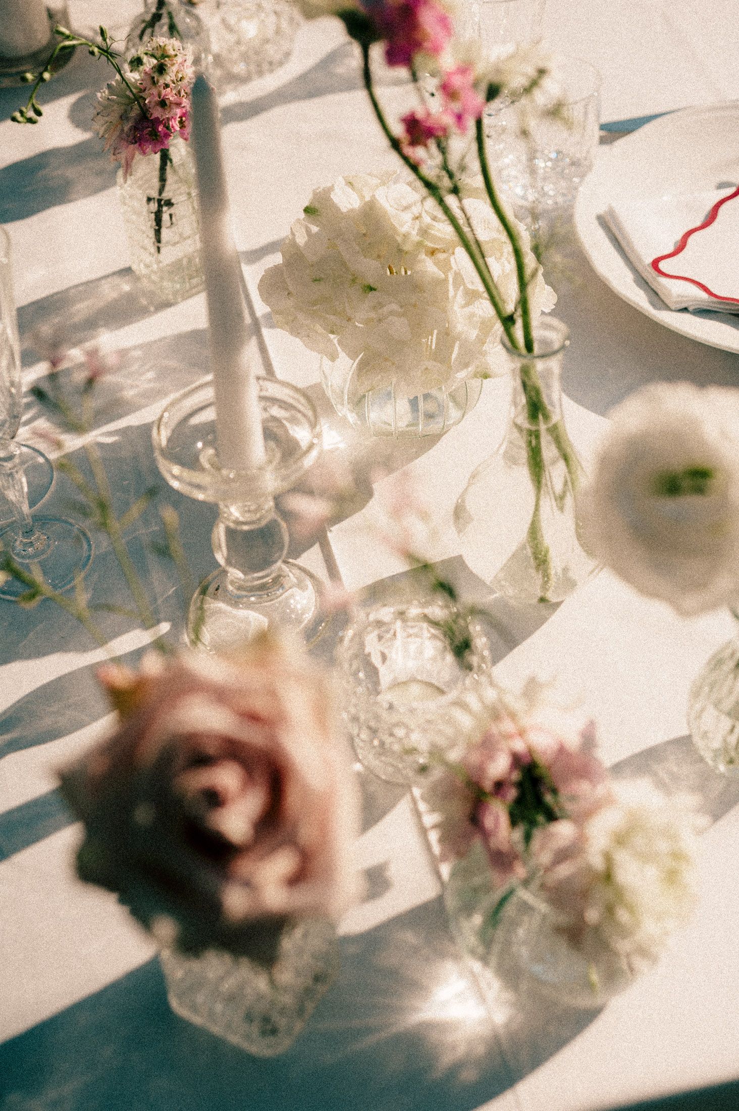 Delicate pink flowers in glass vases cast soft shadows on a white surface with elegant crystal or glass decor nearby.