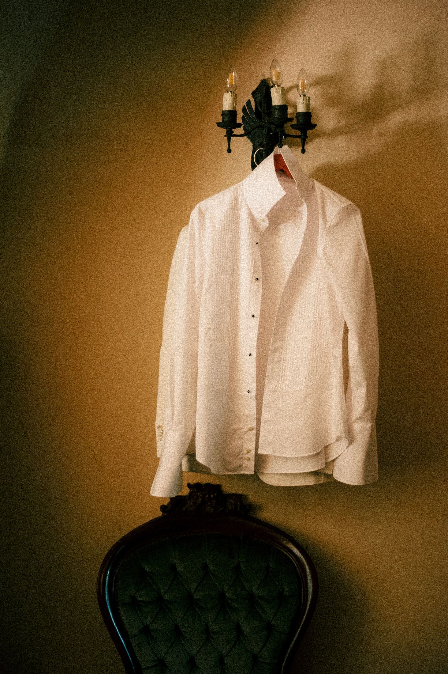 A sequence of white dress shirts arranged on black velvet chairs against a sepia-toned background.