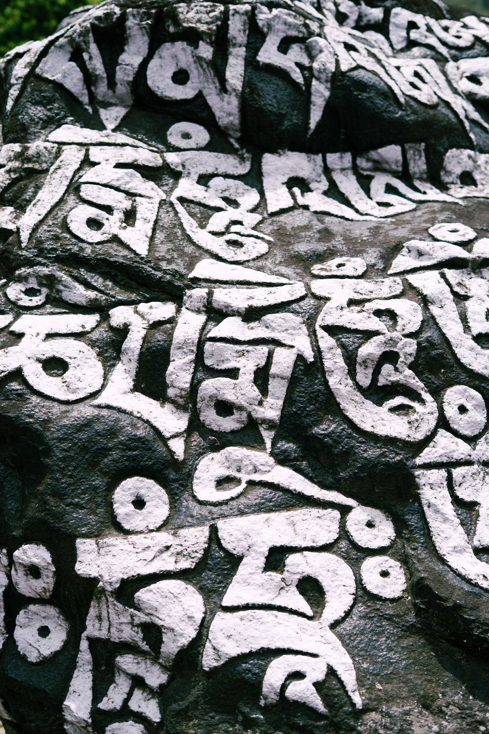 Ancient Tibetan Buddhist mani stones carved with white prayer script against dark rock background.