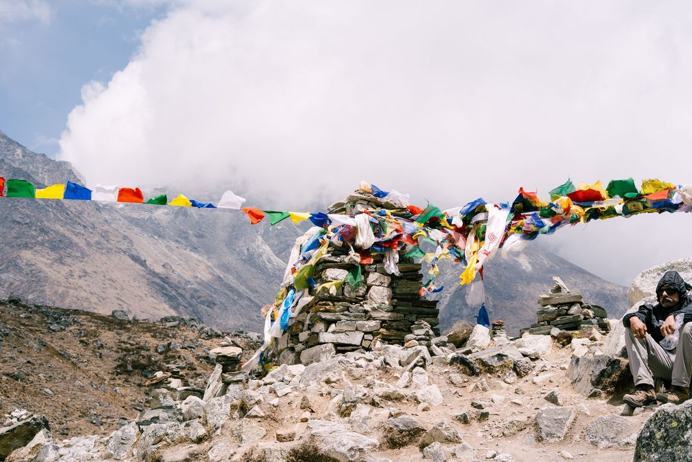 Prayer flags strung across rocky mountainside with snow-capped peaks in distance.