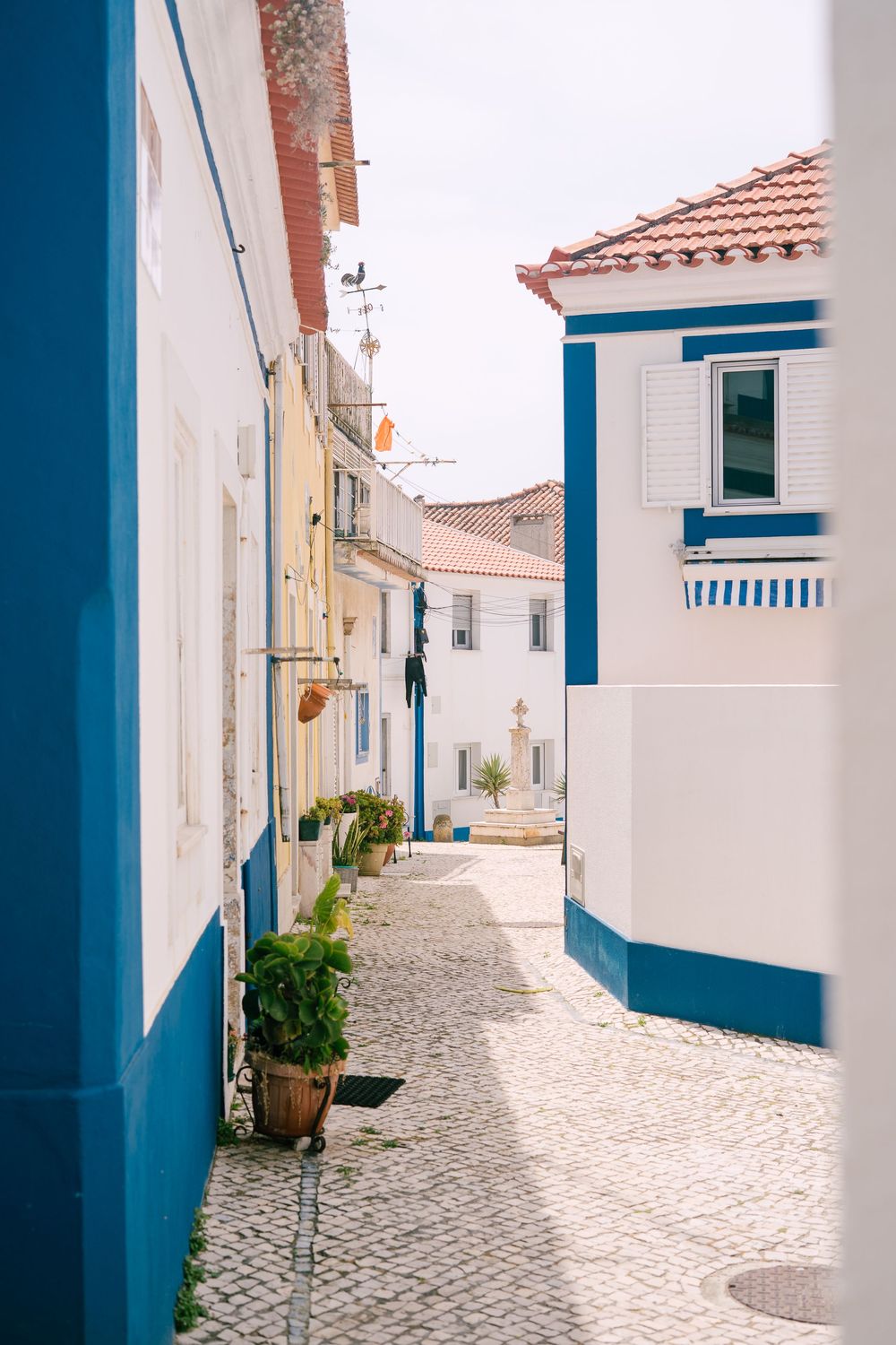 Charming white-washed street with blue trim and cobblestone path in a Mediterranean village.