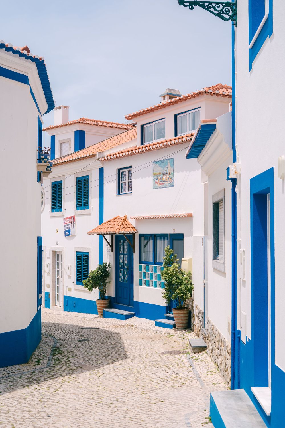 White and blue Portuguese buildings with terracotta roofs along a narrow cobblestone street.