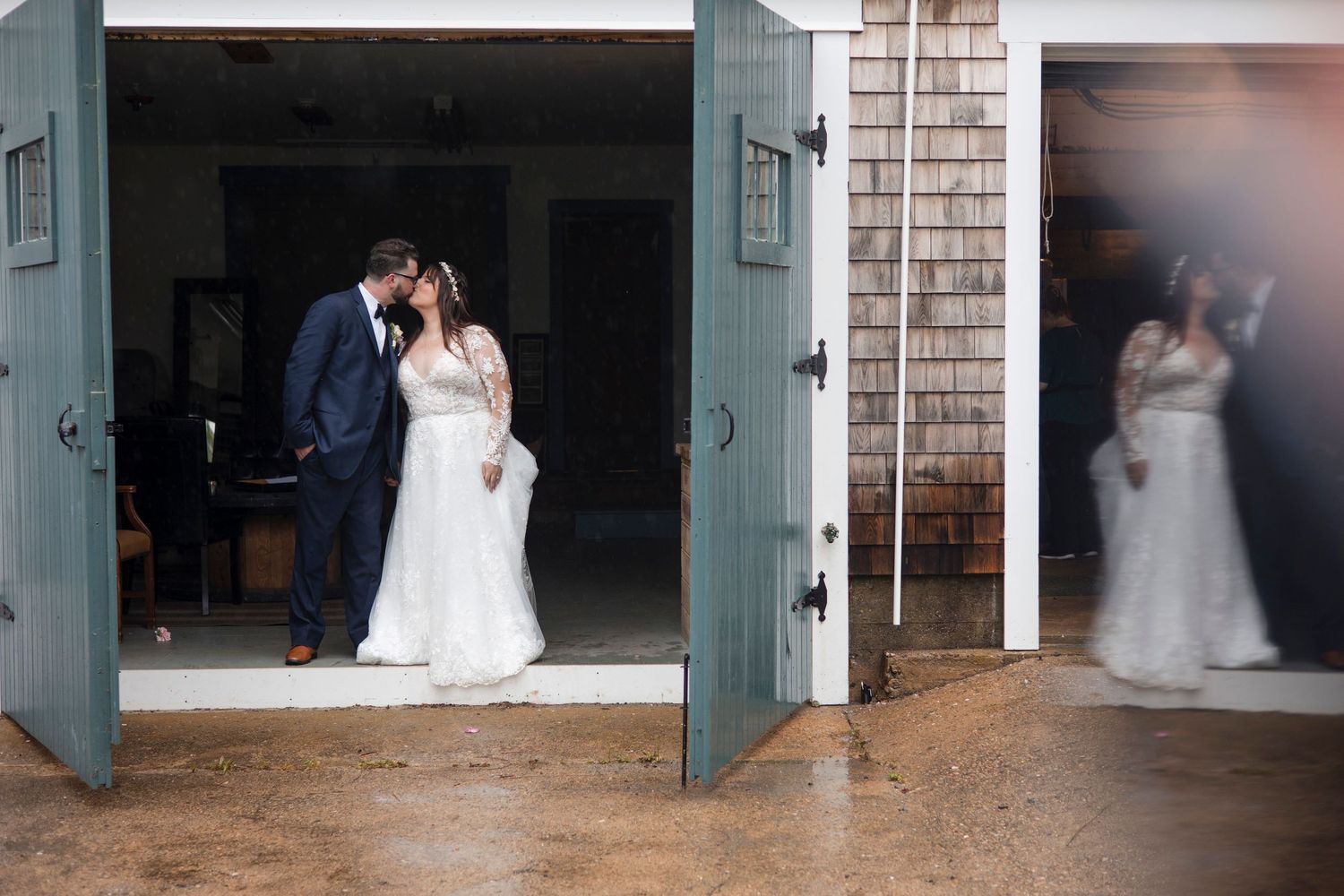 A romantic couple in wedding attire embraces in the doorway of a rustic barn with sage green doors.