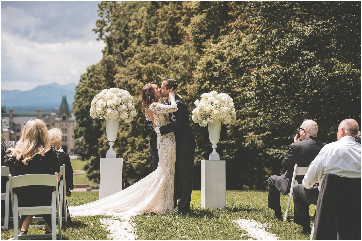A romantic outdoor wedding ceremony overlooking a scenic mountain lake with guests seated in white chairs.