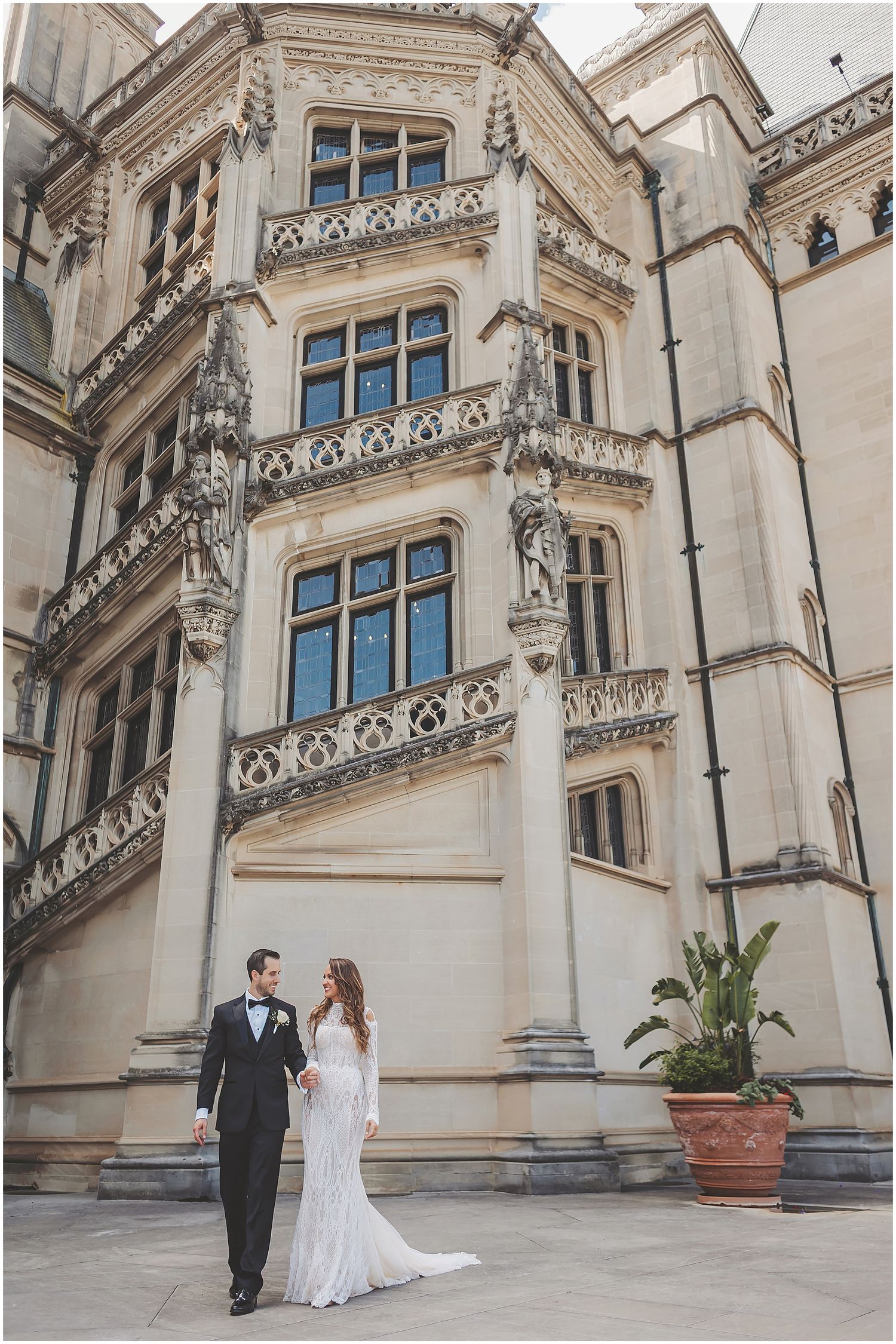 Elegant couple poses against ornate architectural backdrop of historic Biltmore Estate with Gothic stone details and windows.