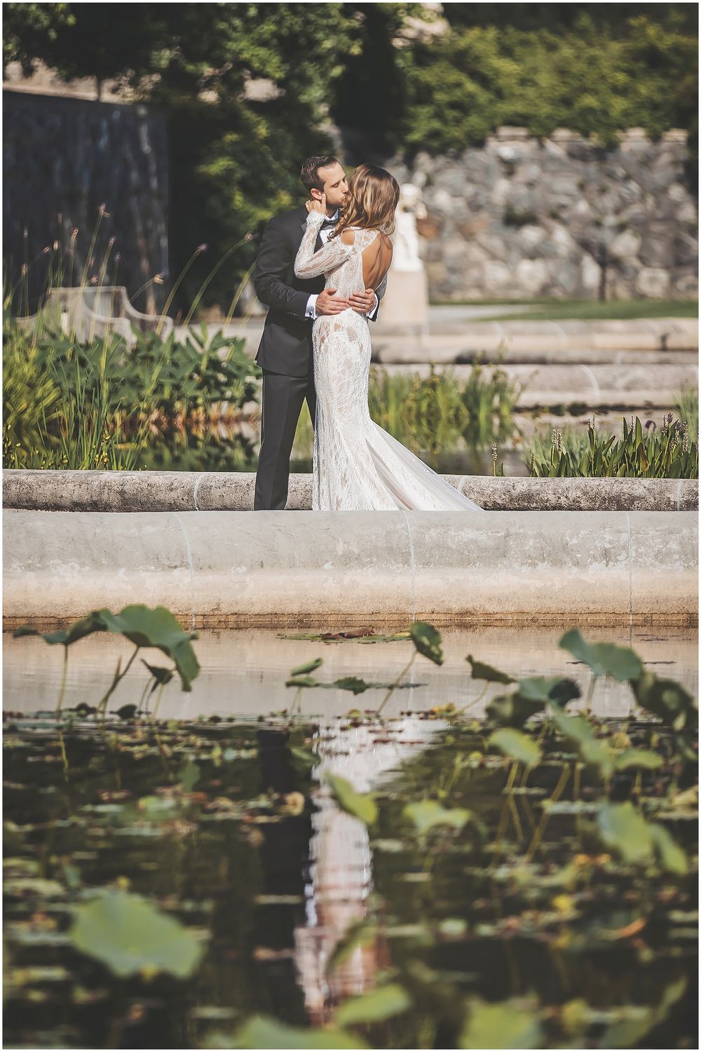 A couple shares a romantic moment near a serene lily pond while capturing their special day in an elegant garden setting.