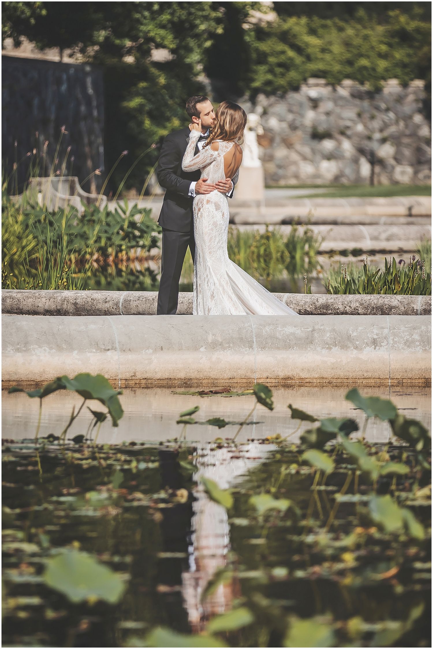A couple shares a romantic moment near a serene lily pond while capturing their special day in an elegant garden setting.