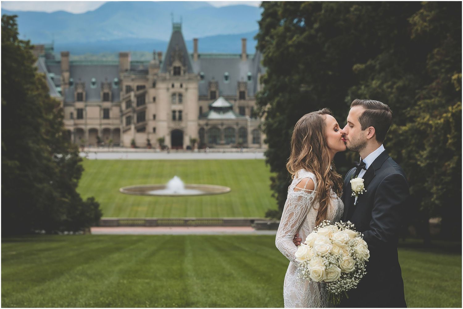 Scenic mountain estate grounds with stone buildings and fountains surrounded by lush gardens and trees in warm daylight.