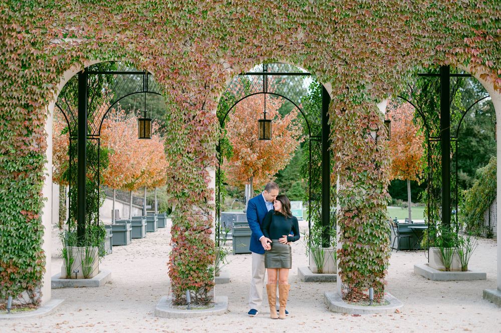 Couple standing beneath ornate ivy-covered garden archways in an elegant architectural setting.