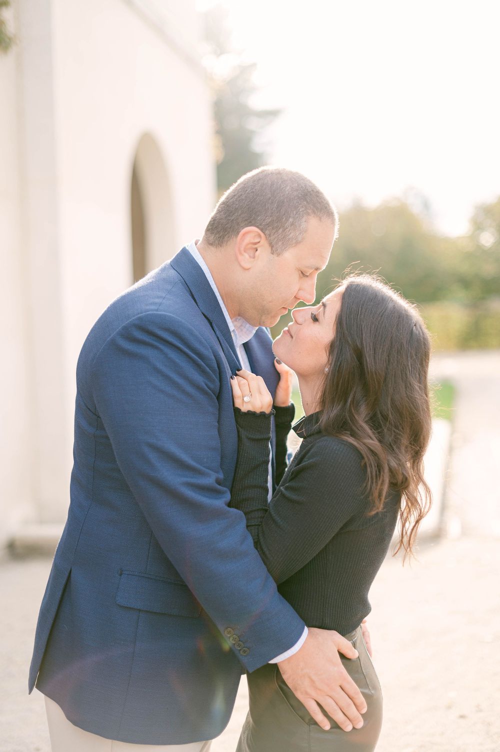 Romantic moment shared between couple in elegant attire against white architectural backdrop.