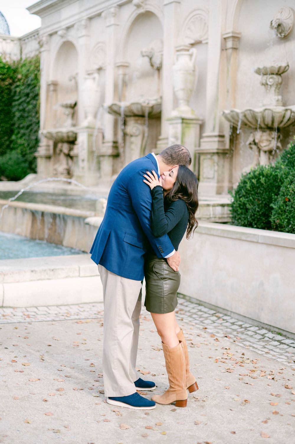 Couple embracing near ornate fountain wall with classical architectural details.