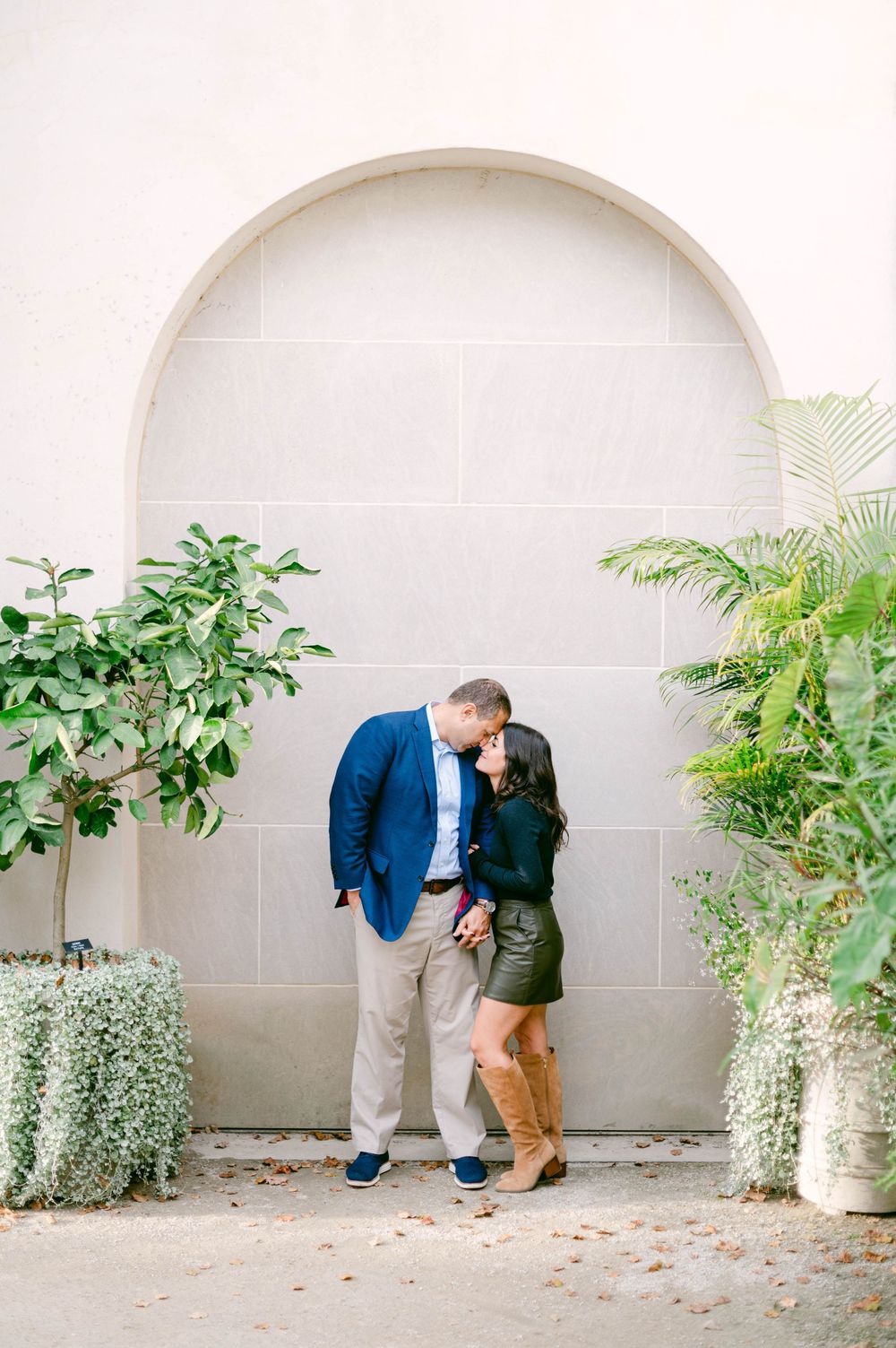 Intimate moment captured against neutral arched wall surrounded by lush greenery.