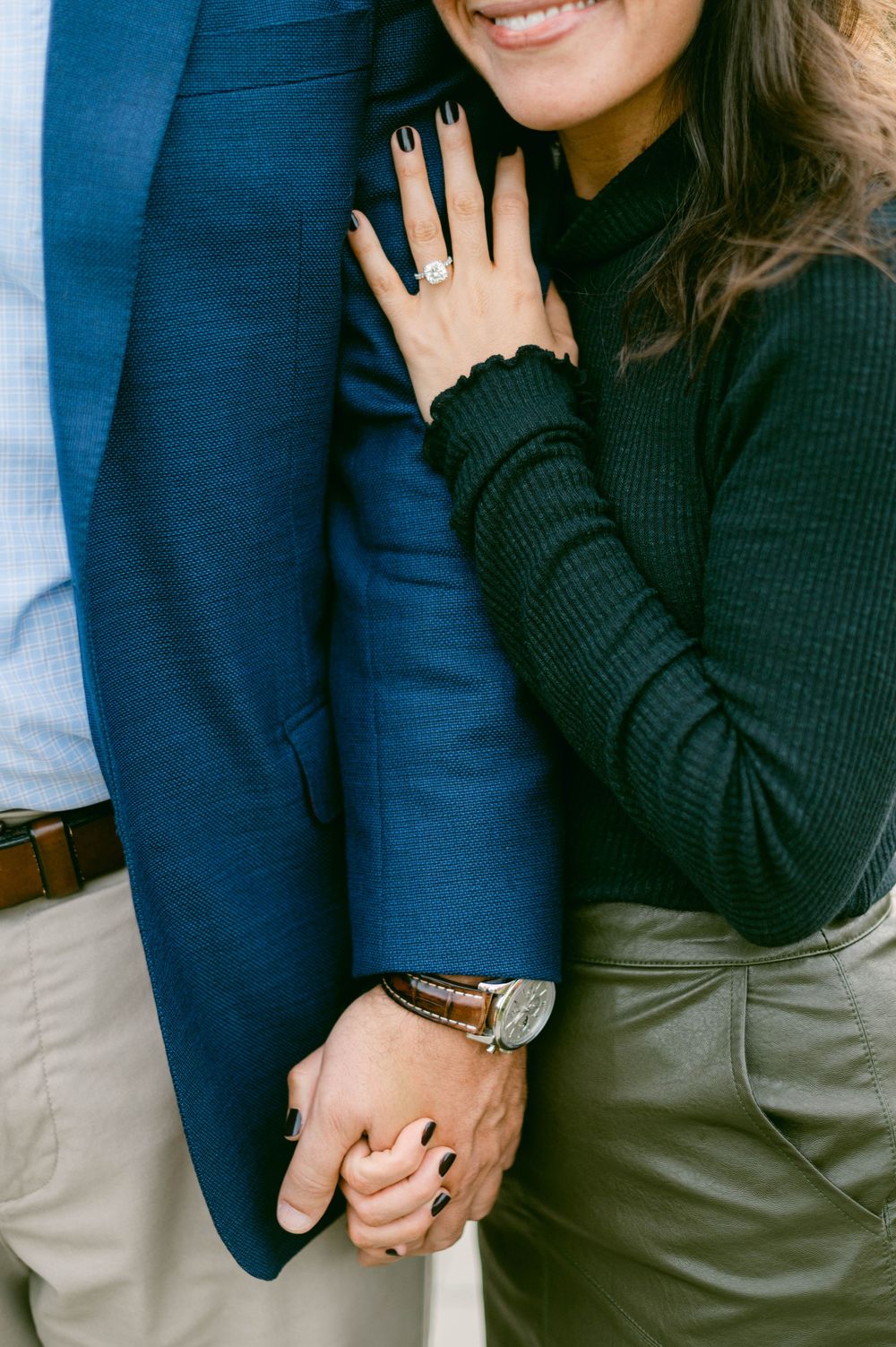 Close-up of engagement ring and loving embrace showing formal attire details.
