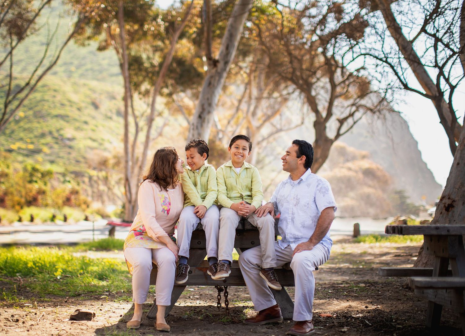 Family dressed in white and pastel colors enjoying time together on park bench.