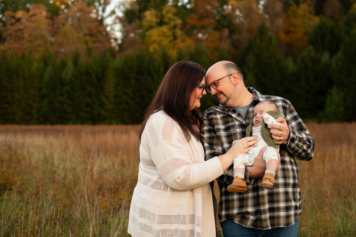 A couple shares an intimate moment while holding drinks in a fall field at sunset.