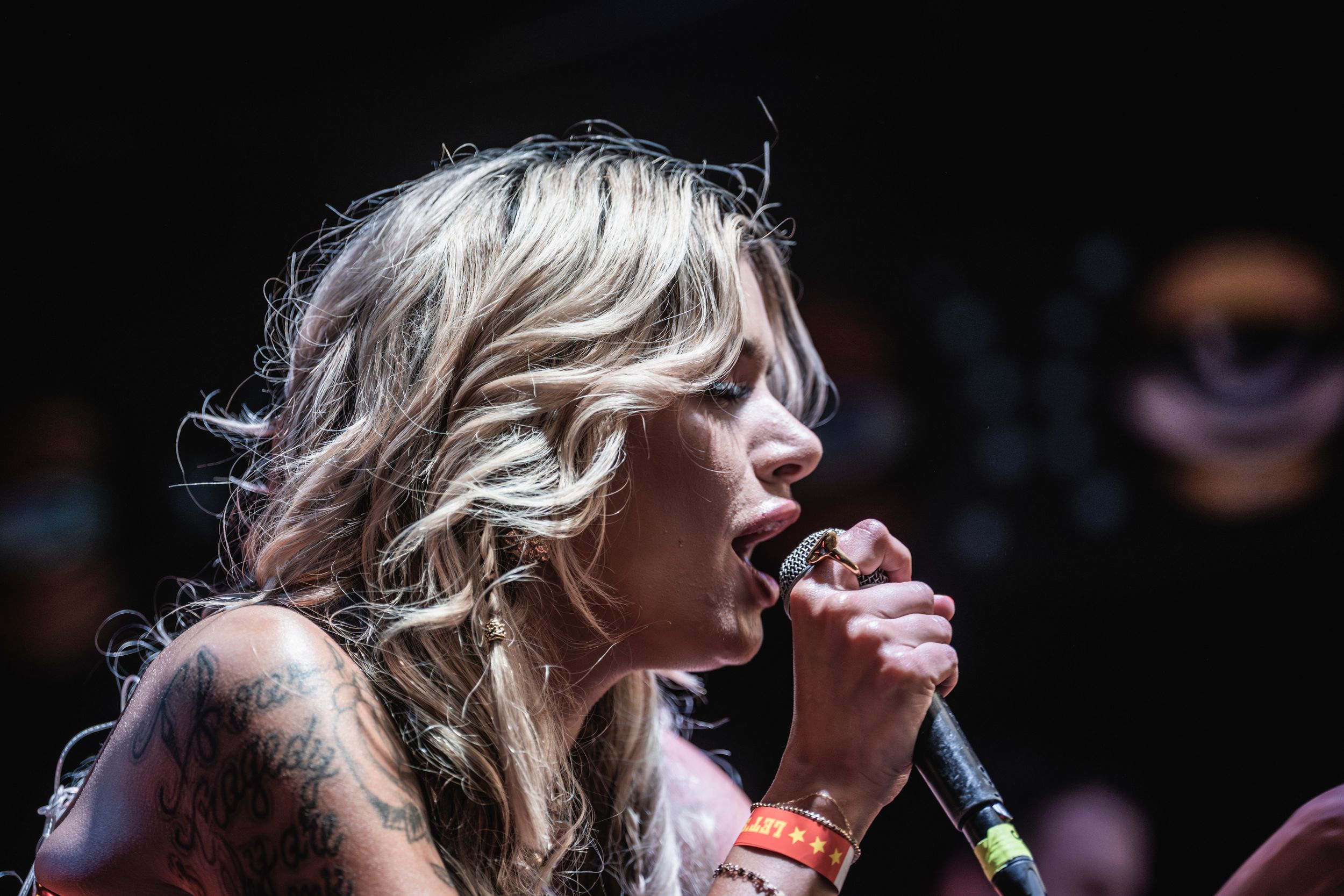 Multiple people harmonizing together while performing on stage with microphones in a dark concert setting.