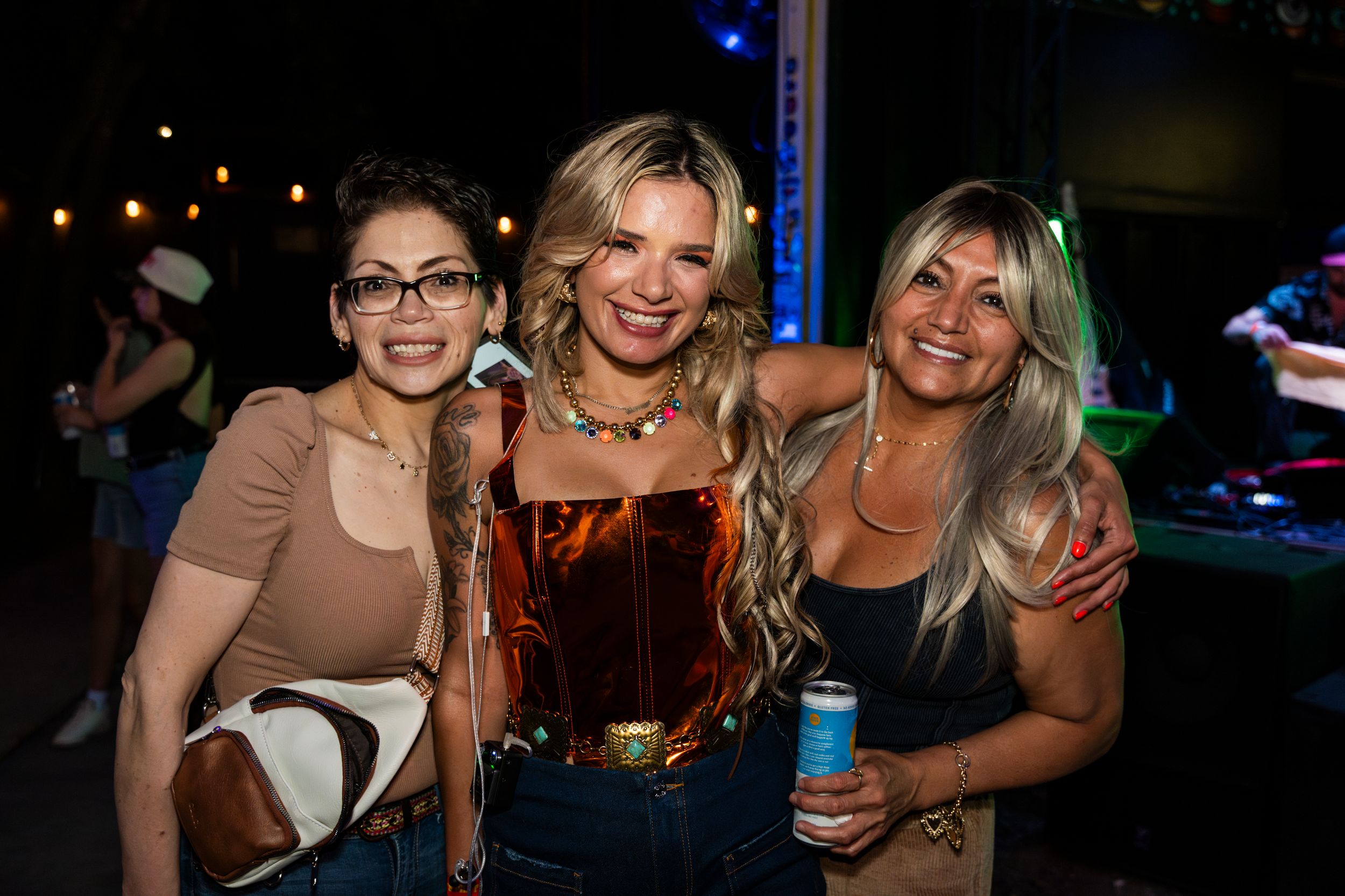 Three friends pose together smiling at a nightclub with blue lighting in the background.