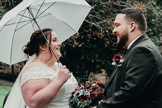 A happy moment shared between a couple during their wedding ceremony under a white umbrella with autumn foliage in background.