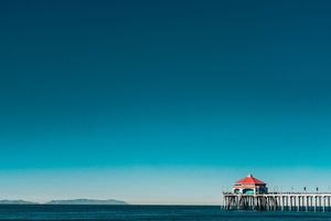 Scenic ocean pier with red-roofed pavilion extending over calm blue waters against a vibrant turquoise sky.