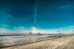 Panoramic view of a pier extending over calm ocean waters under a bright blue sky.