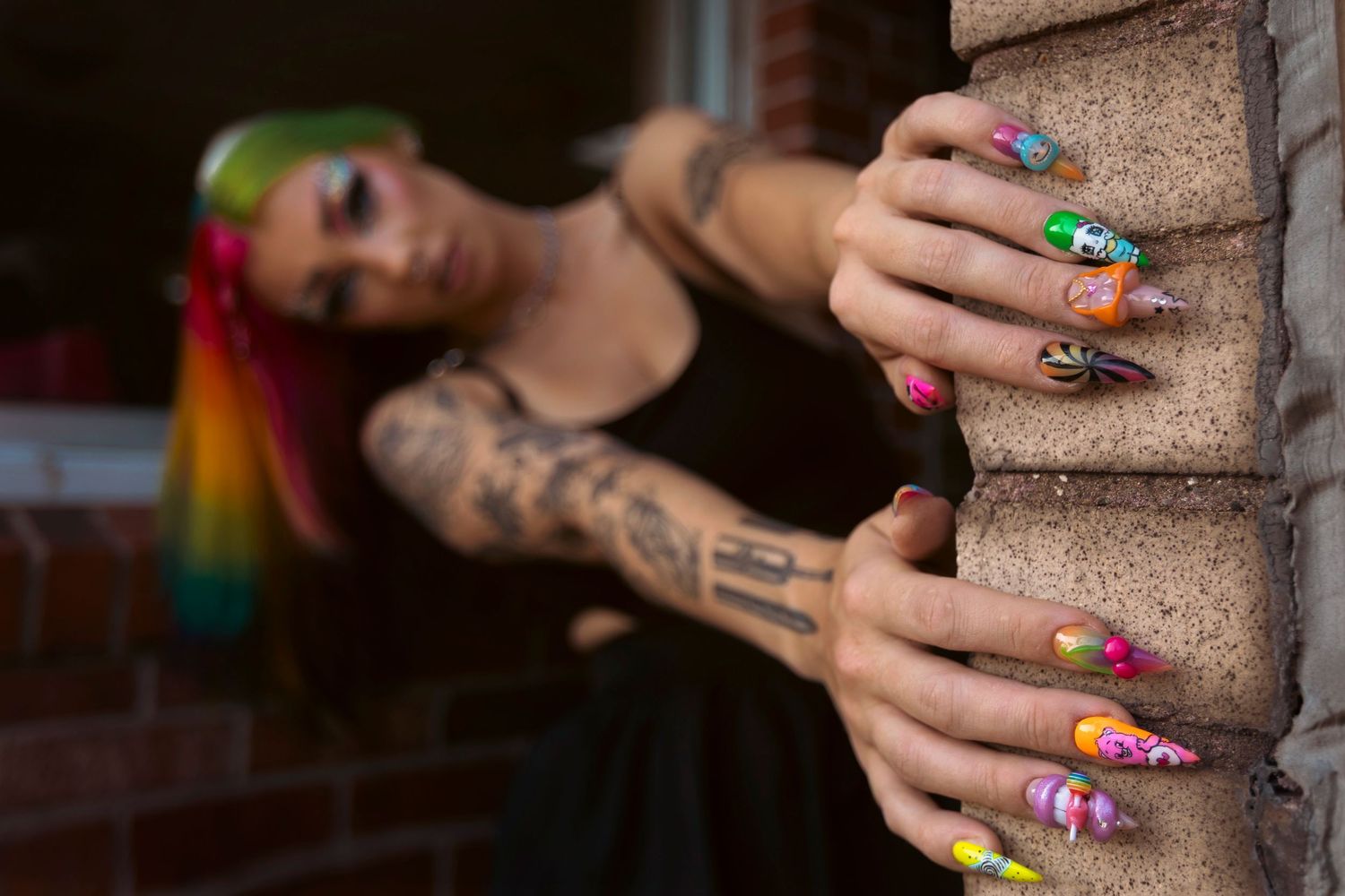 Hands with vibrant rainbow-colored fingernails grip a textured surface in multiple close-up shots.